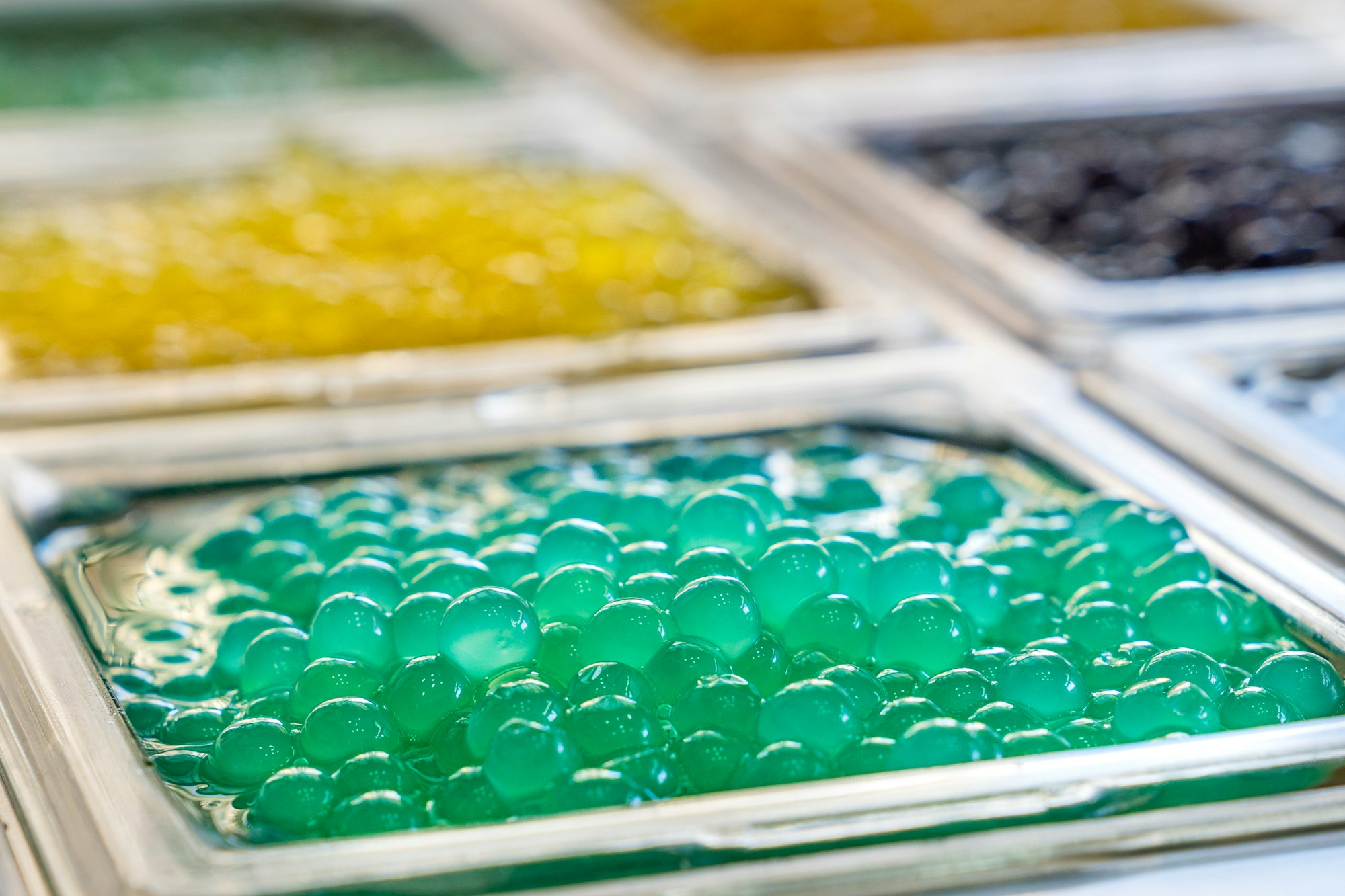 Green bobas piled up in the toppings window of a bubble drinks store. Close up